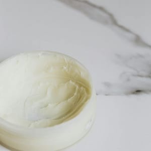 Close-up of a skincare cream in a round container on a marble surface.