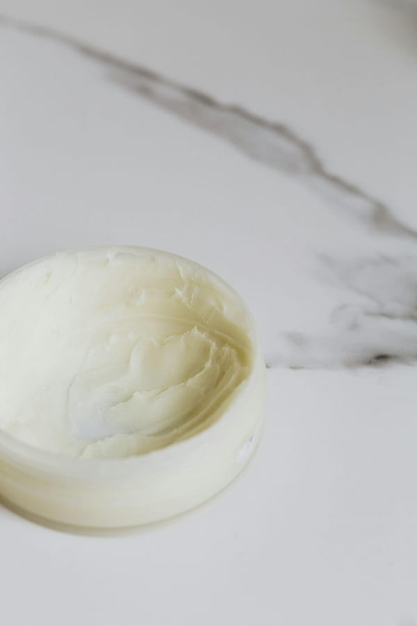 Close-up of a skincare cream in a round container on a marble surface.